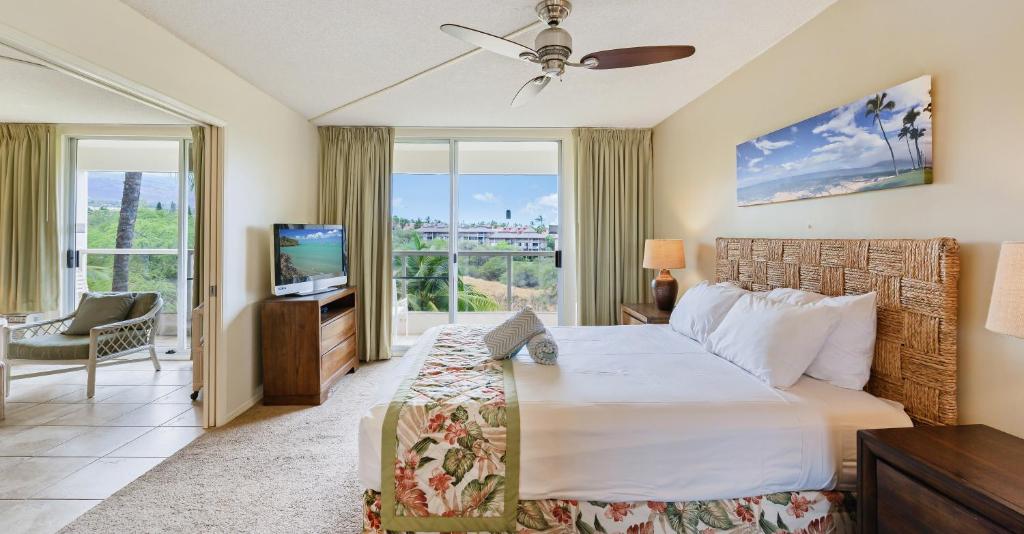 a bedroom with a bed and a tv and a balcony at Castle at Maui Banyan in Wailea