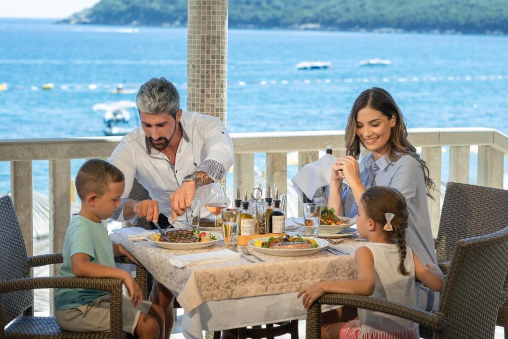 a family eating food at a table on the beach at Poseidon The Beach Hotel in Budva