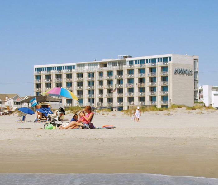 a group of people sitting on the beach in front of a hotel at Acropolis Oceanfront Resort in North Wildwood