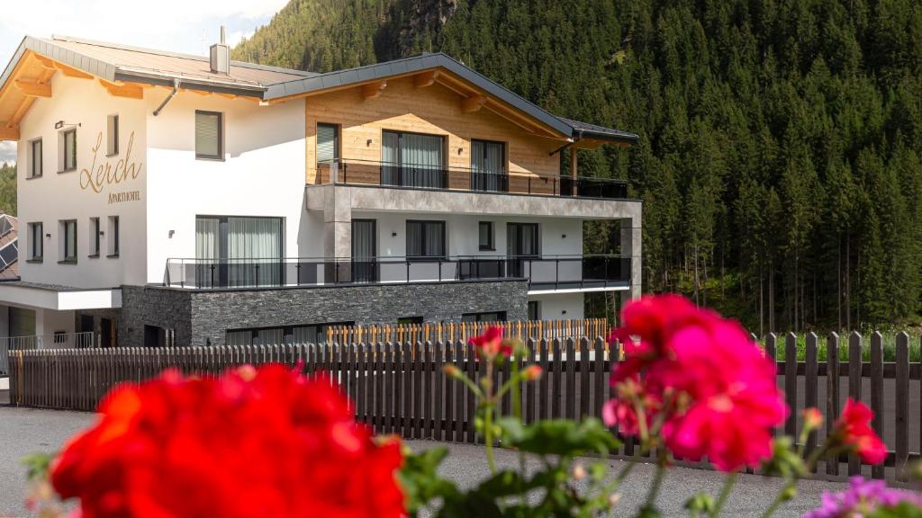 ein Haus mit einem Zaun und roten Blumen in der Unterkunft Aparthotel Lerch in Kappl