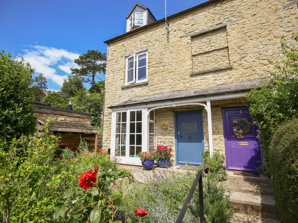 a brick house with a purple door and flowers at Weavers Cottage in Nailsworth