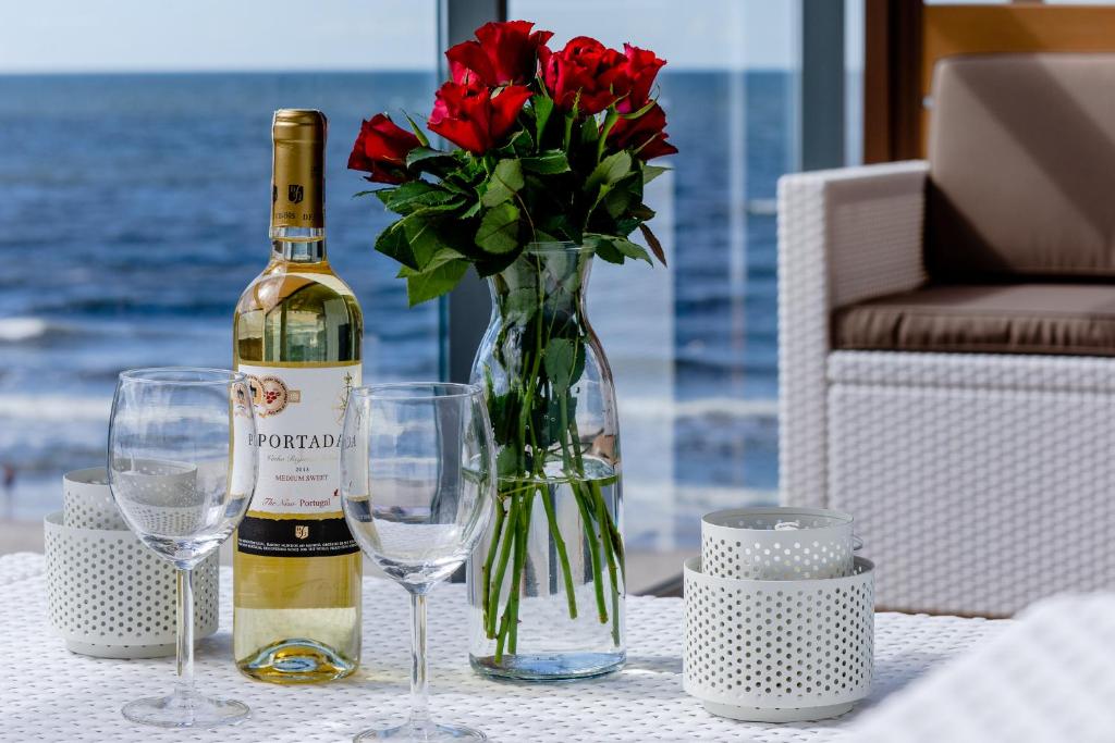 a bottle of wine and a vase with red roses at Apartament BŁĘKITNY Gardenia Dziwnów z widokiem na morze EPapartamenty in Dziwnów