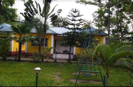 Una casa amarilla con una escalera delante. en Jaldapara Inn Resort en Mādāri Hāt