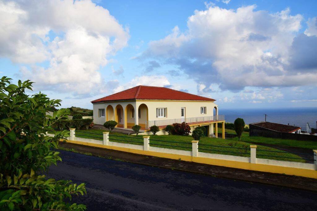 a white house with a red roof in front of the ocean at Casa dos cinco sentidos in Feteira Pequena
