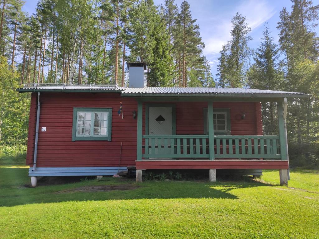 ein kleines rotes Haus mit einer Veranda im Gras in der Unterkunft Ekesberget Stugby stuga 10 in Ekshärad