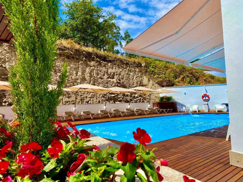 a swimming pool with red flowers and umbrellas at Harpazul in Catoira