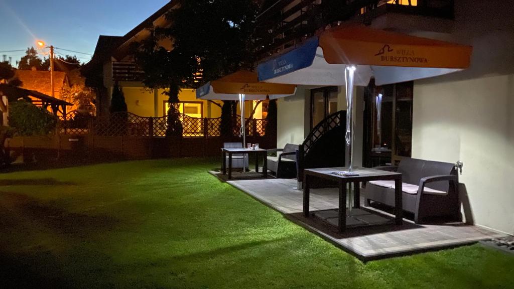 a patio with two tables and umbrellas on a lawn at Willa Bursztynowa in Kąty Rybackie