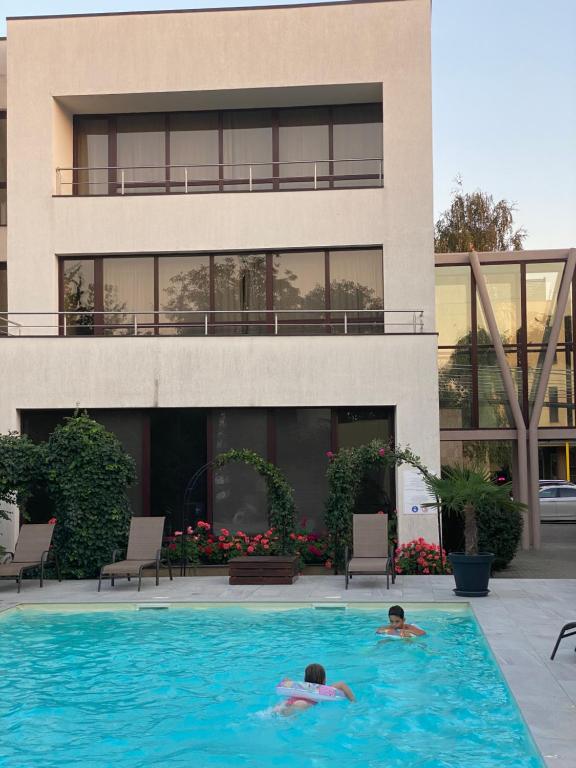 2 persone che nuotano in una piscina di fronte a un edificio di Hotel Perla a Timişoara