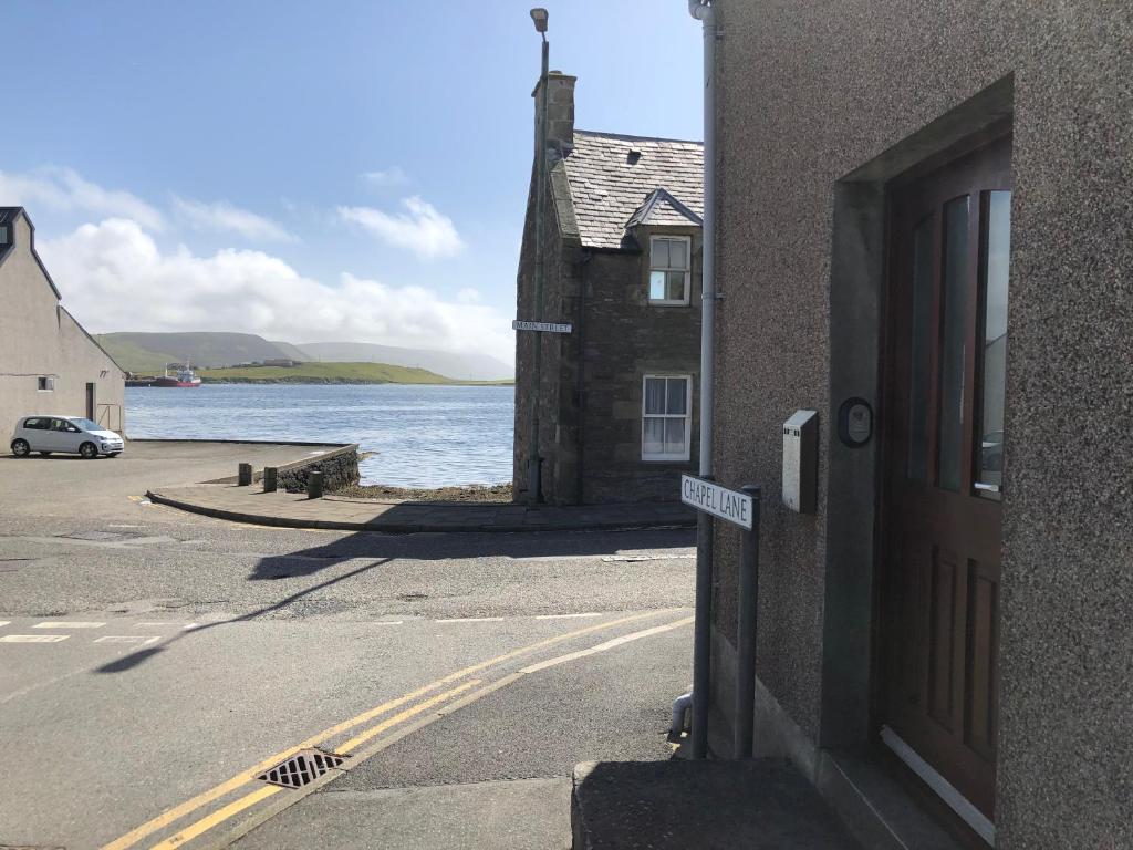 a building on the side of a road next to a body of water at Cosy holiday home, Scalloway, Shetland. in Scalloway