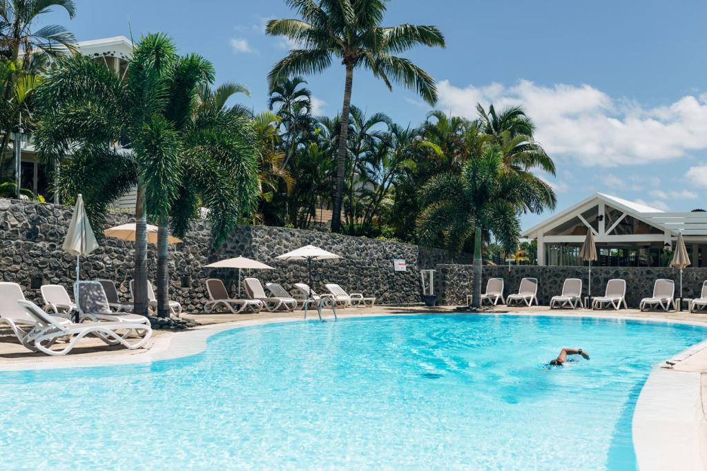 a person swimming in a pool with chairs and palm trees at Résidence l'Archipel in Saint-Gilles les Bains