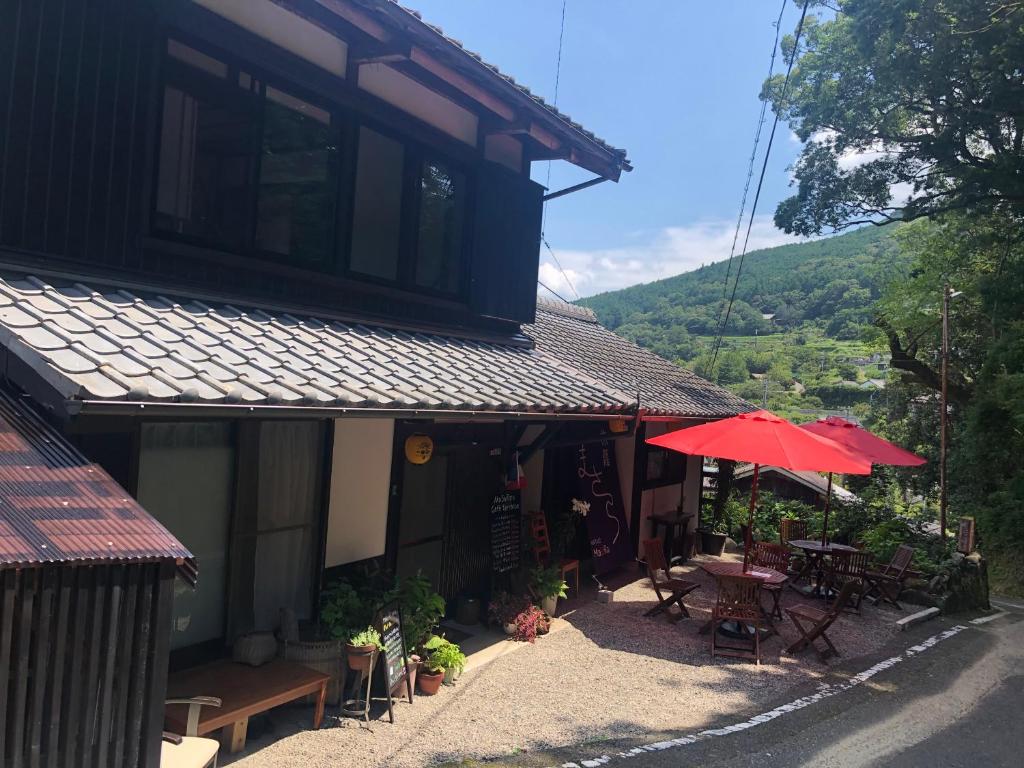 een gebouw met een rode paraplu en tafels en stoelen bij 旅籠まさら HATAGO MaSaRa in Tanabe