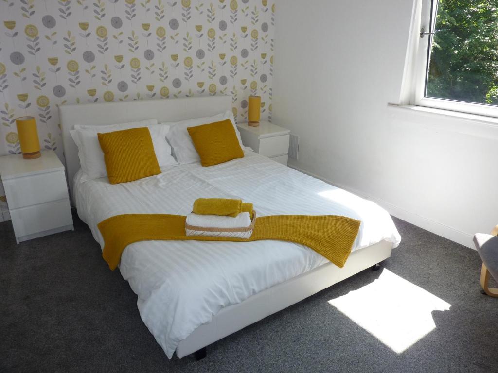a bedroom with a white bed with yellow pillows and a window at Paisley Central Apartment #4 in Paisley