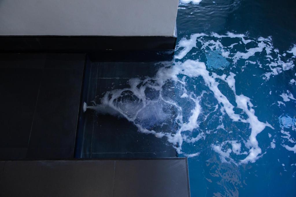 A close-up shows moving blue water beside the pool’s dark tiled edge and steps.