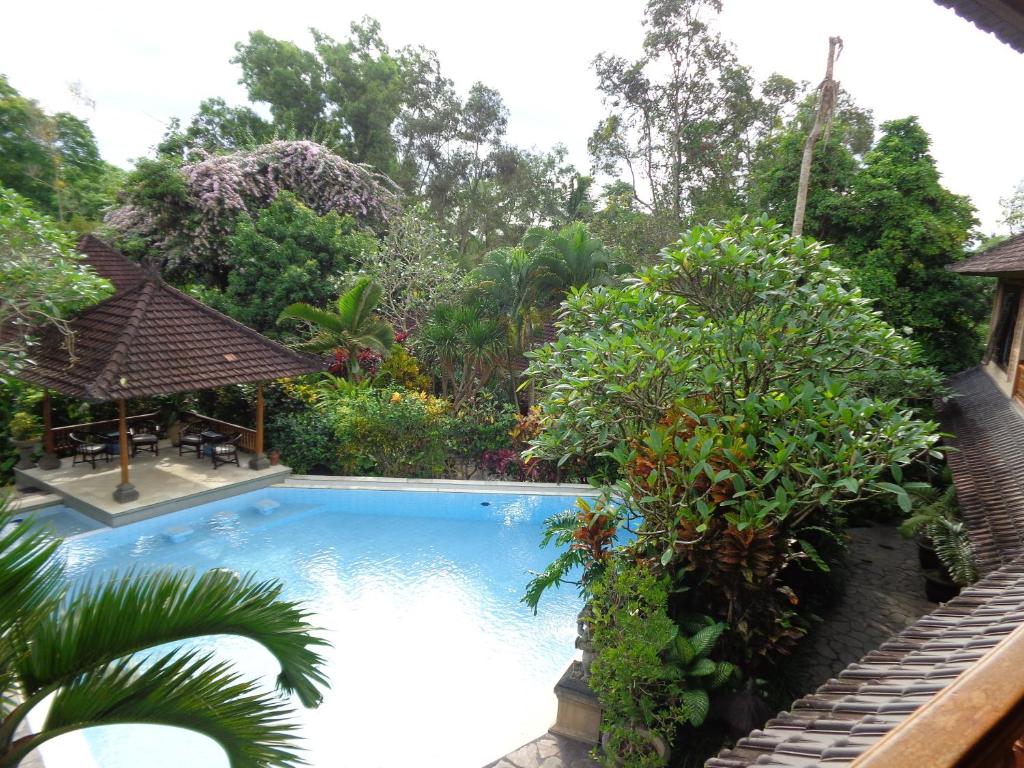 a swimming pool in a garden with trees at Klub Kokos Bungalows in Ubud