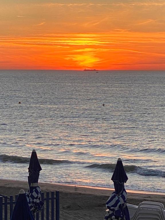 a sunset on the beach with two chairs and the ocean at Manoir de la Marjolaine in Cabourg