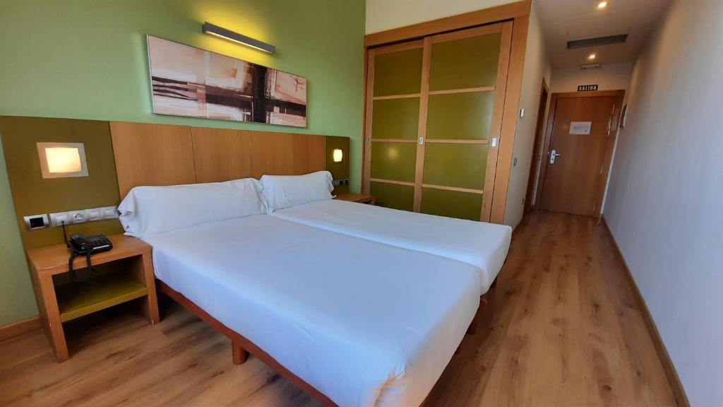 a bedroom with a large white bed and a wooden floor at Hotel La Boroña in Gijón
