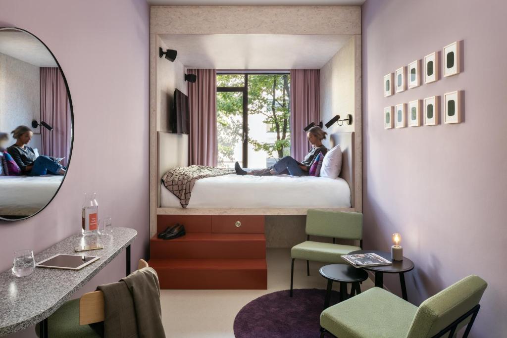 una ragazza seduta su un letto in una stanza con uno specchio di Hotel Unplugged a Rotterdam