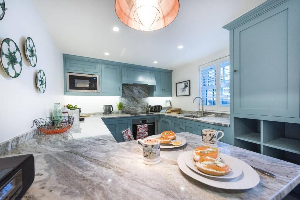 uma cozinha com armários azuis e pratos de comida num balcão em The Garth 5 Star Gold Luxury Cottages em St. Ives