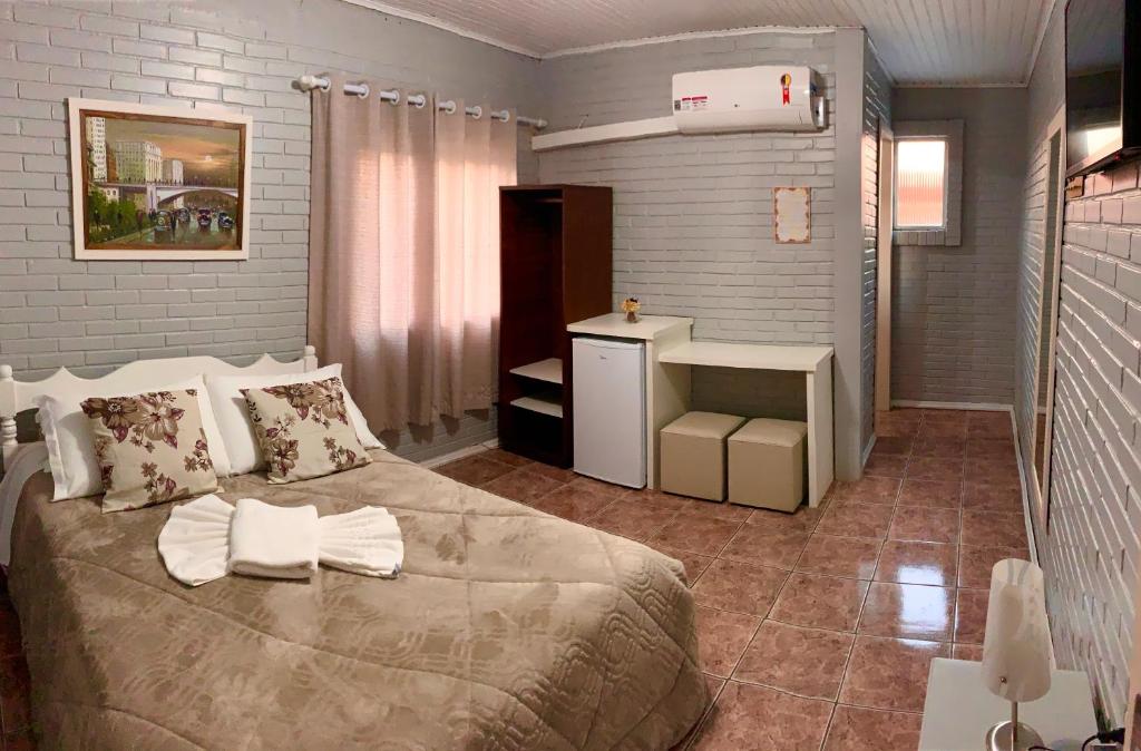 a bedroom with a large bed and a small refrigerator at Pousada Bello Outono in Canela