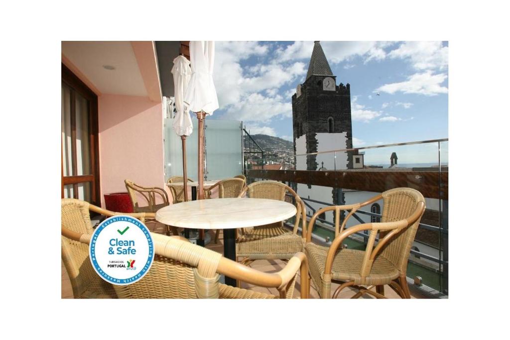 einen Tisch und Stühle auf einem Balkon mit einem Uhrturm in der Unterkunft Hotel Catedral in Funchal