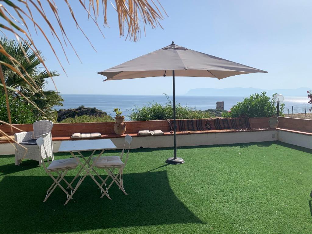 uma mesa e cadeiras com um guarda-sol num relvado em villa vista mare spiaggia privata em Scopello