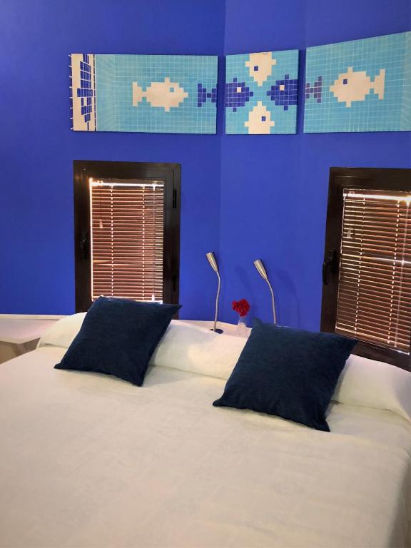a bedroom with a bed with blue walls and two windows at Hostal Alhambra in Zahora
