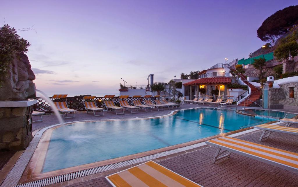 a swimming pool with chairs and the ocean in the background at Parco Residence La Rosa in Ischia