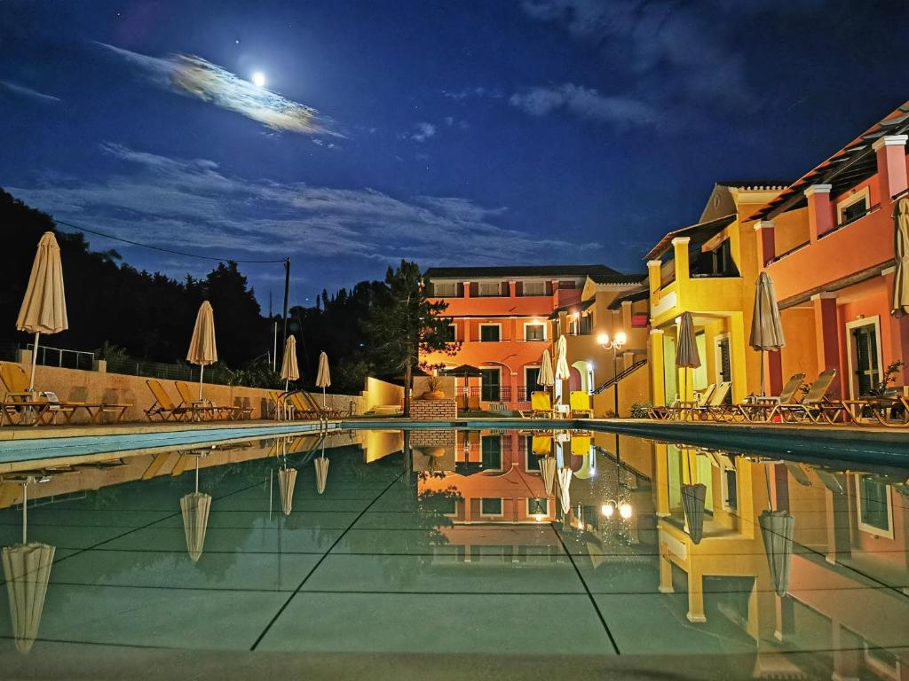 a swimming pool with chairs and umbrellas at night at Sellas Hotel in Sidari