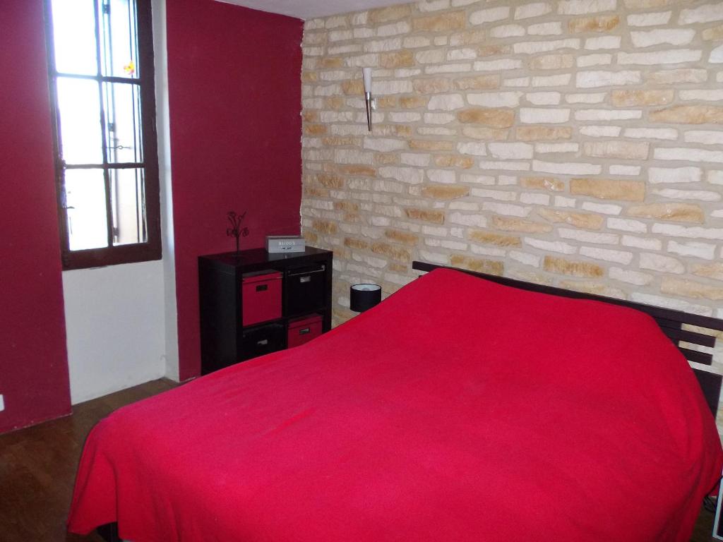 uma cama vermelha num quarto com uma parede de tijolos em Maison atypique à Cordes-Sur-Ciel 2 chambres em Cordes-sur-Ciel