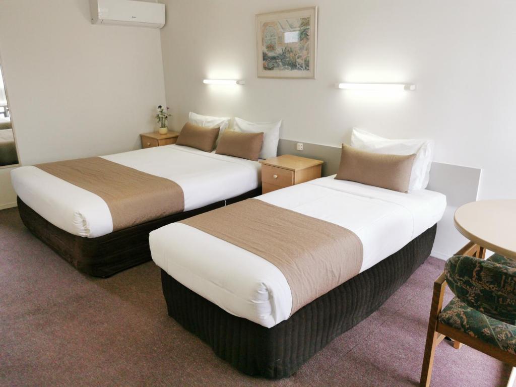 two beds in a hotel room with a table and chairs at Ballarat Eureka Lodge Motel in Ballarat