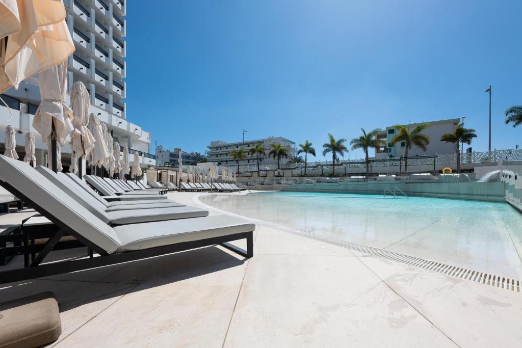 een zwembad met ligstoelen en stoelen naast een gebouw bij Hotel Caserio in Playa del Inglés