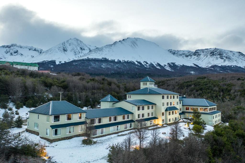 a large building with snow covered mountains in the background at Los Acebos Ushuaia Hotel in Ushuaia