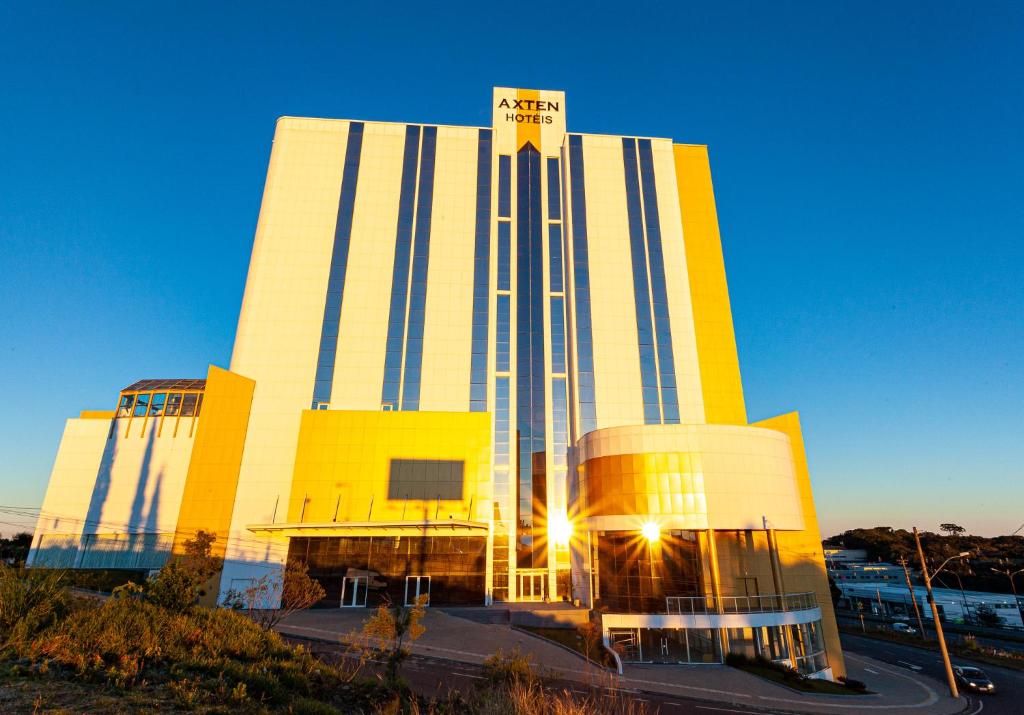 um grande edifício amarelo e branco com o sol brilhando sobre ele em Travel Inn Axten Caxias do Sul em Caxias do Sul