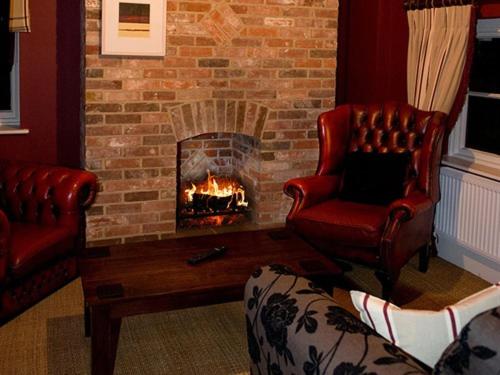 sala de estar con chimenea de ladrillo y 2 sillas en Brasteds Lodge, en Norwich