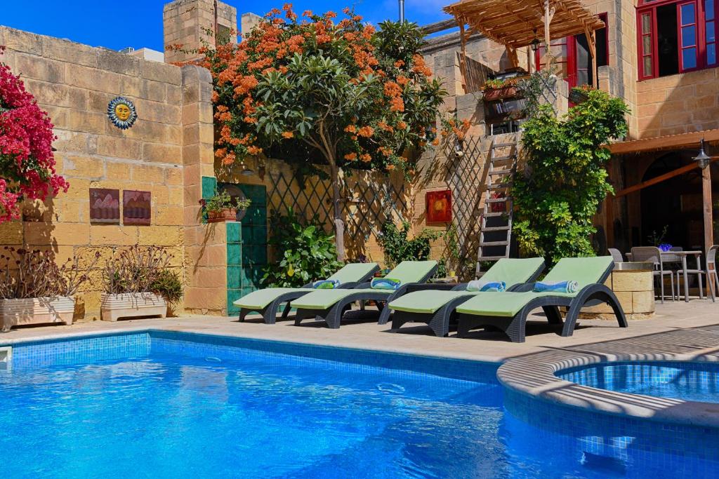 a swimming pool with green lounge chairs next to a building at Charming B&B Dar Ta Zeppi in Qala