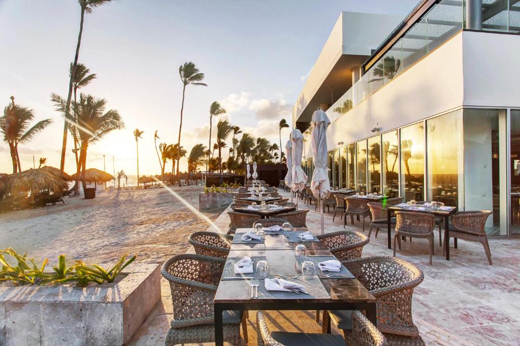 Beachfront dining area with tables set for service, umbrellas, sand, and ocean view.