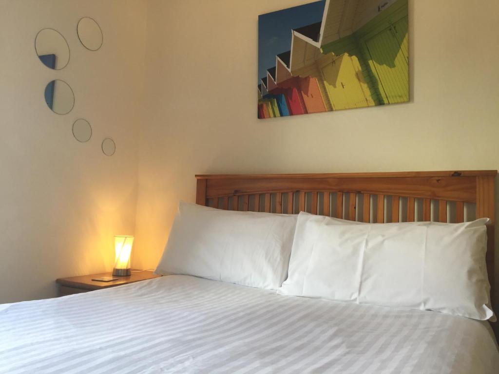 Barbican Reach Guest House في بلايموث: سرير بملاءات بيضاء ومصباح على طاولة