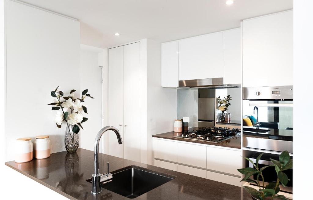 RNR Serviced Apartments North Melbourne في ملبورن: مطبخ مع دواليب بيضاء ومغسلة مع ورد