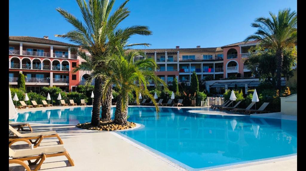 une grande piscine avec des palmiers en face d'un hôtel dans l'établissement Appartement de standing face à la baie de St-Tropez, vue mer, jardin et piscine., à La Garonnette-Plage
