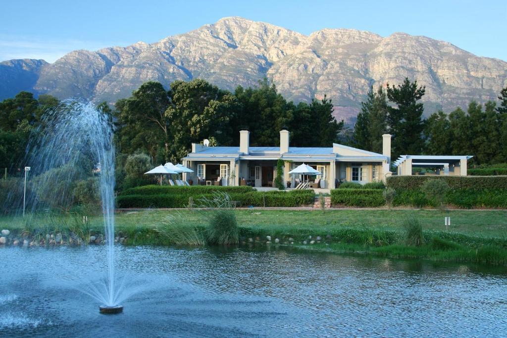 a fountain in the middle of a pond with a house at La Cabriere Country House in Franschhoek