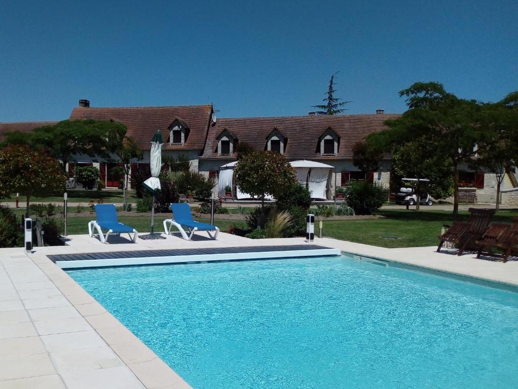 a swimming pool with two blue chairs and a house at Camping Au Clos de Beaulieu in Bossée