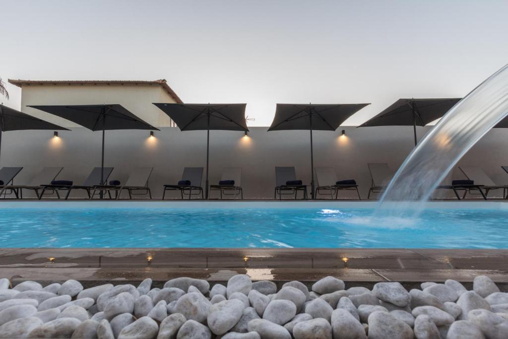 a fountain in a pool with chairs and umbrellas at Giafra Luxury Rooms in Agrigento