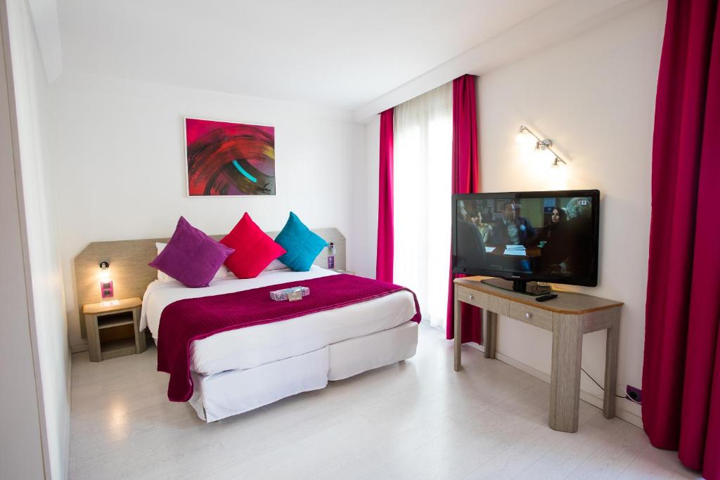 a bedroom with a bed with red curtains and a television at Cristal Hôtel & Spa in Cannes