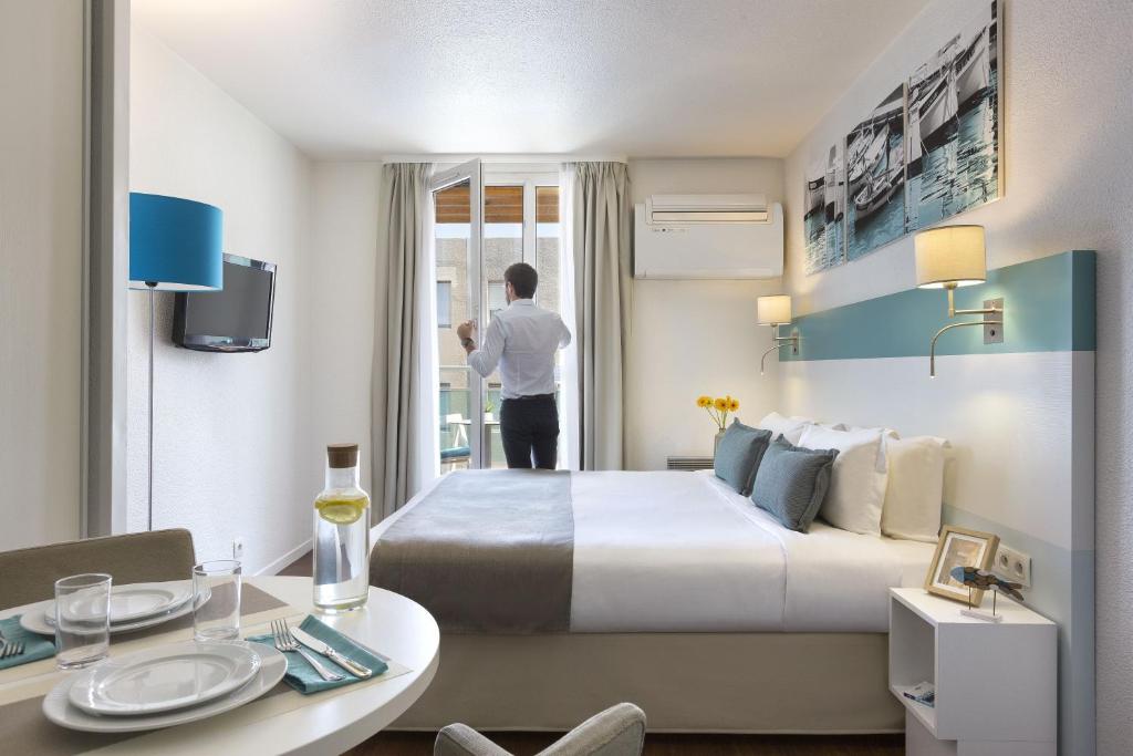 un hombre mirando por la ventana de una habitación de hotel en Citadines Castellane Marseille en Marsella