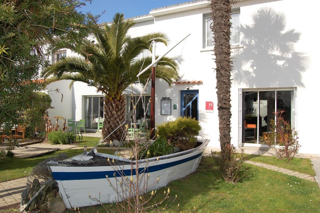 ein Boot vor einem Haus mit einer Palme in der Unterkunft Hotel Le Goeland in Barbâtre