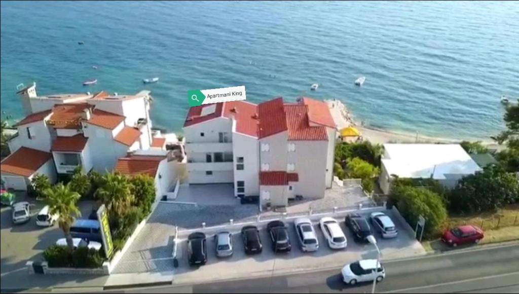 a building with cars parked in a parking lot next to the ocean at APARTMENTS KING 2 in Podstrana