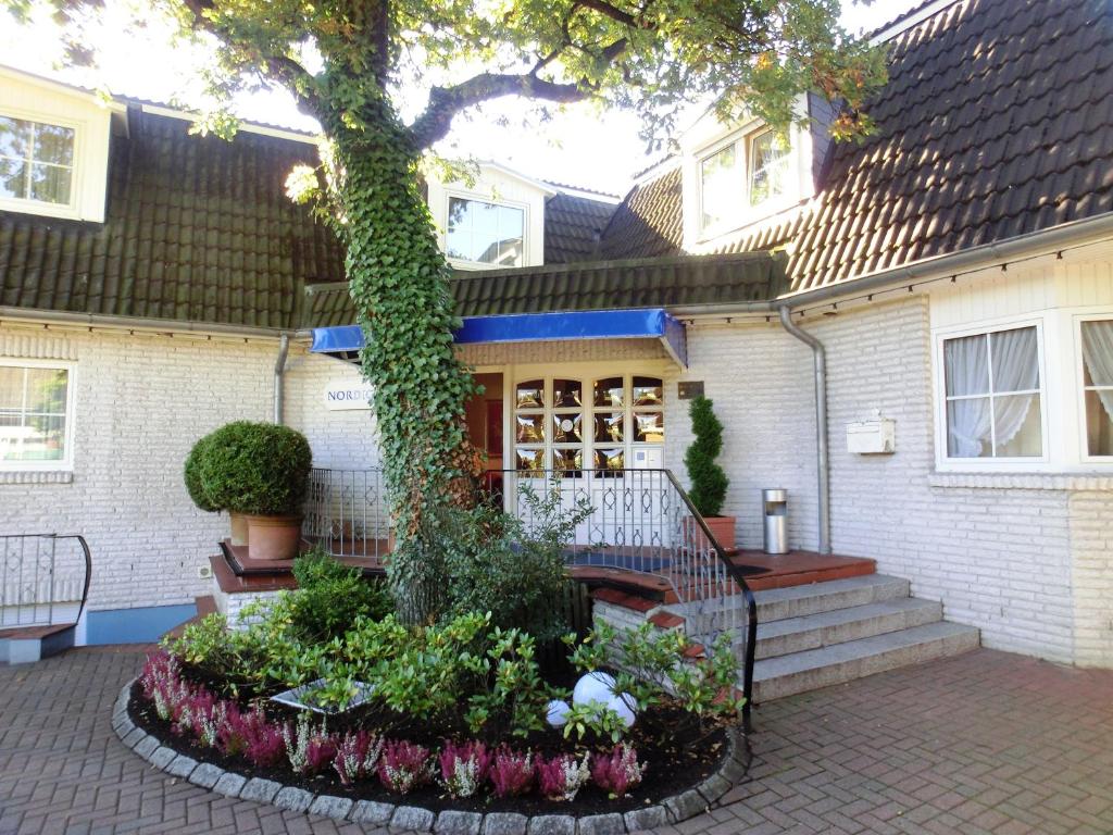 a tree in front of a house with a garden at Hotel Nordic in Norderstedt