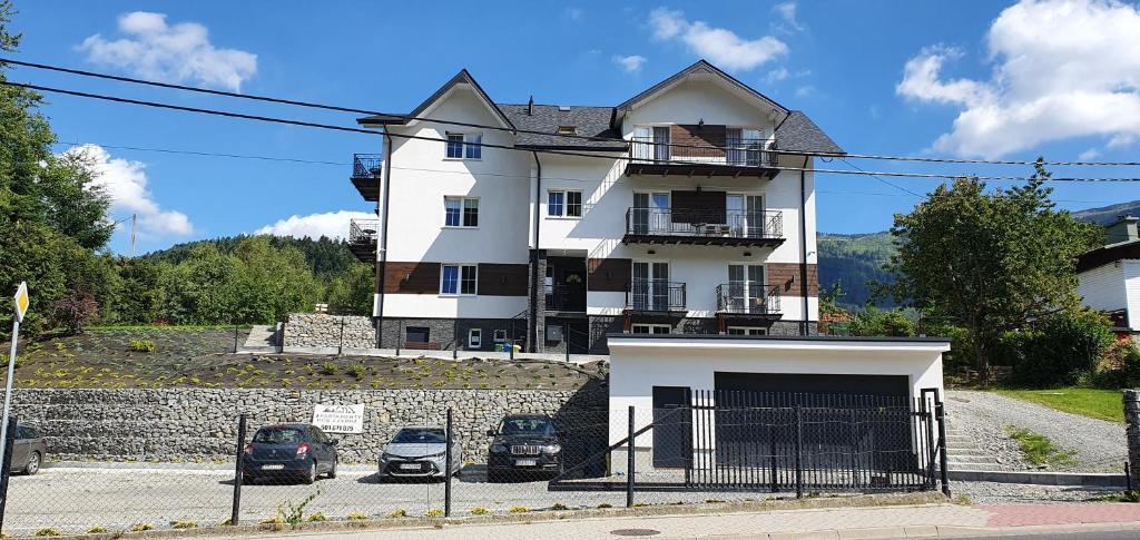 Biały dom z samochodami zaparkowanymi przed nim w obiekcie Apartamenty pod Czyrną w Szczyrku