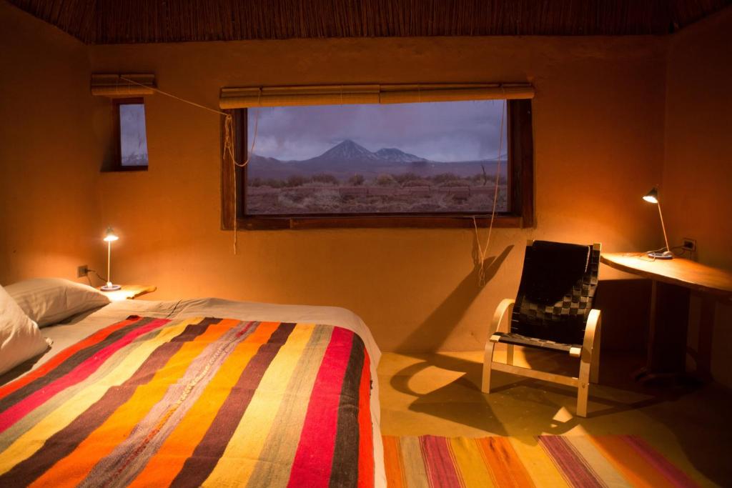 a bedroom with a bed and a chair and a window at Planeta Atacama Lodge in San Pedro de Atacama