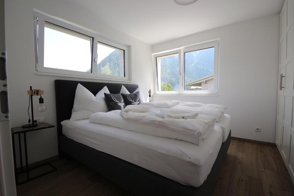 a bedroom with a large white bed with two windows at Bellevue Apartments in Bürserberg